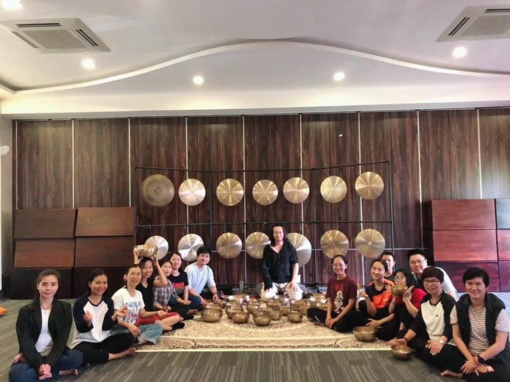 Câu Chuyện Của Chúng Tôi 26 Nhóm người ngồi trước bức tường gắn chiêng lớn.