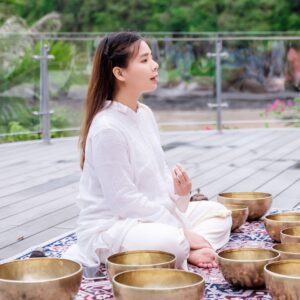 Trị Liệu Chuông Xoay Và Yoga Tại Cát Bà 2 Người phụ nữ thiền bên cạnh bát chuông vàng.