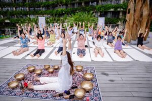 Trị Liệu Chuông Xoay Và Yoga Tại Cát Bà 12 Người tập yoga ngoài trời, tay giơ cao