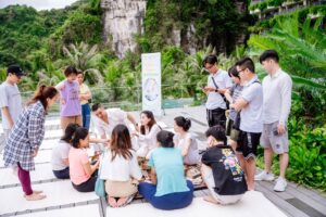 Trị Liệu Chuông Xoay Và Yoga Tại Cát Bà 30 Nhóm người tham gia hoạt động ngoài trời, nơi nhiều cây xanh.