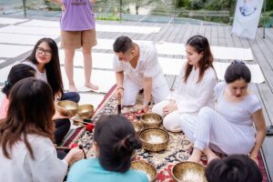 Trị Liệu Chuông Xoay Và Yoga Tại Cát Bà 33 Nhóm người ngồi tập yoga với bát hát Tây Tạng.