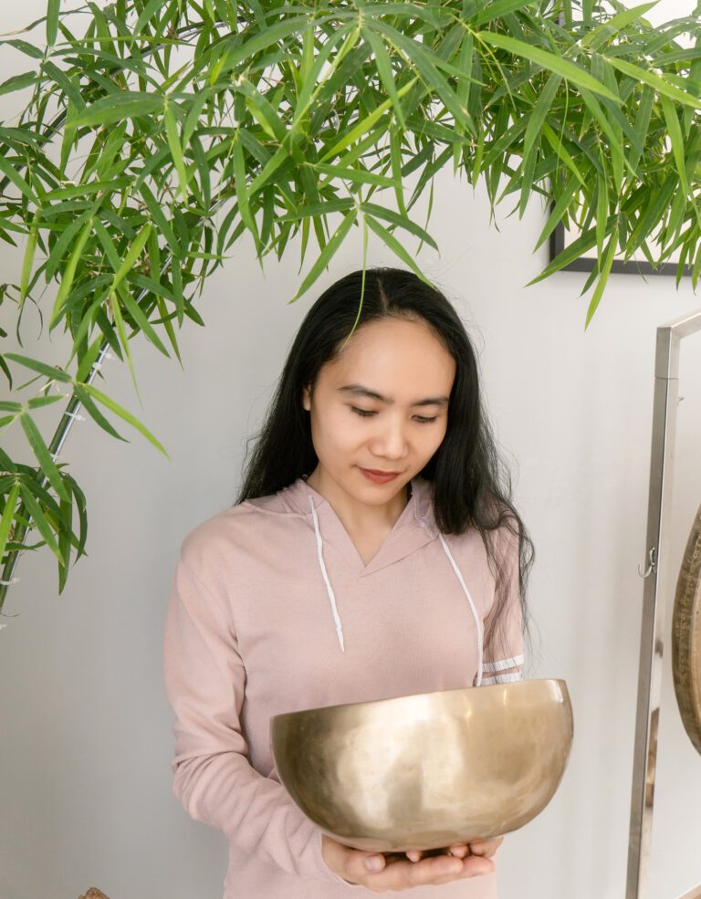 Người phụ nữ cầm chuông đồng dưới cây xanh.