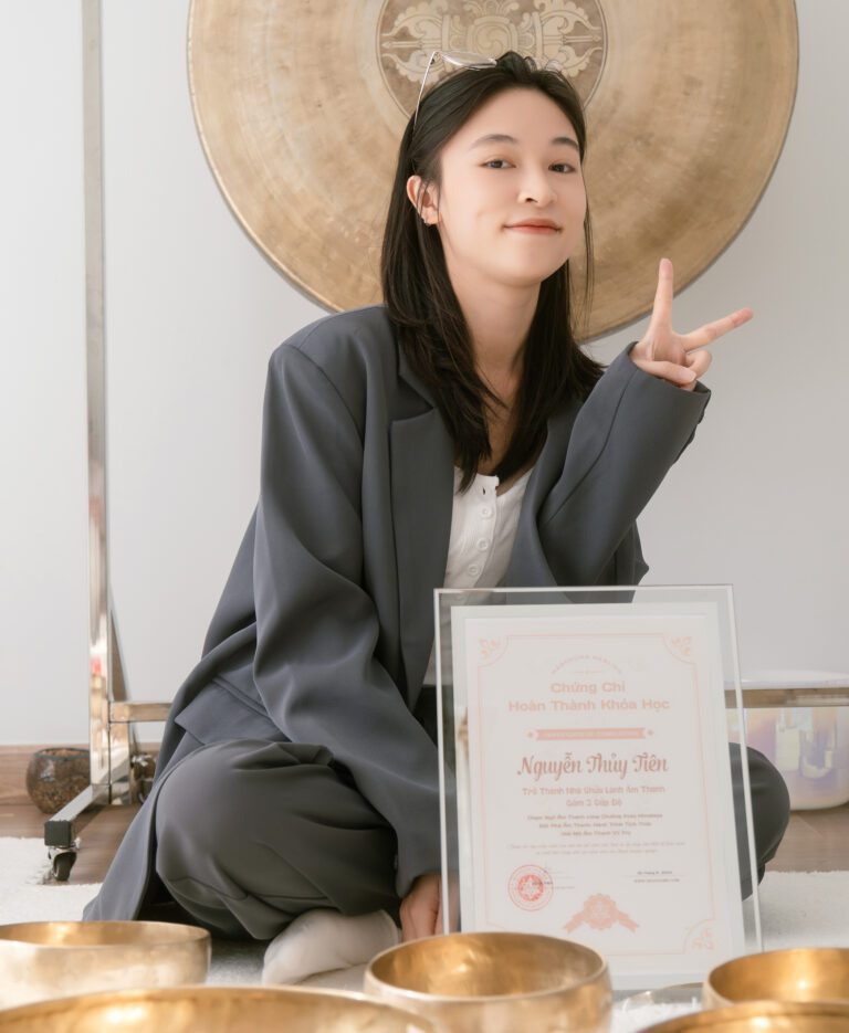 Người phụ nữ cầm chứng chỉ, biển đồng phía sau.