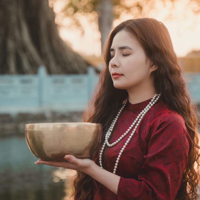 Người phụ nữ cầm chuông xoay himalaya đồng, mặc áo dài đỏ.