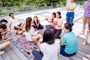 Người ngồi thiền bên bát đồng lớn trên sàn gỗ.